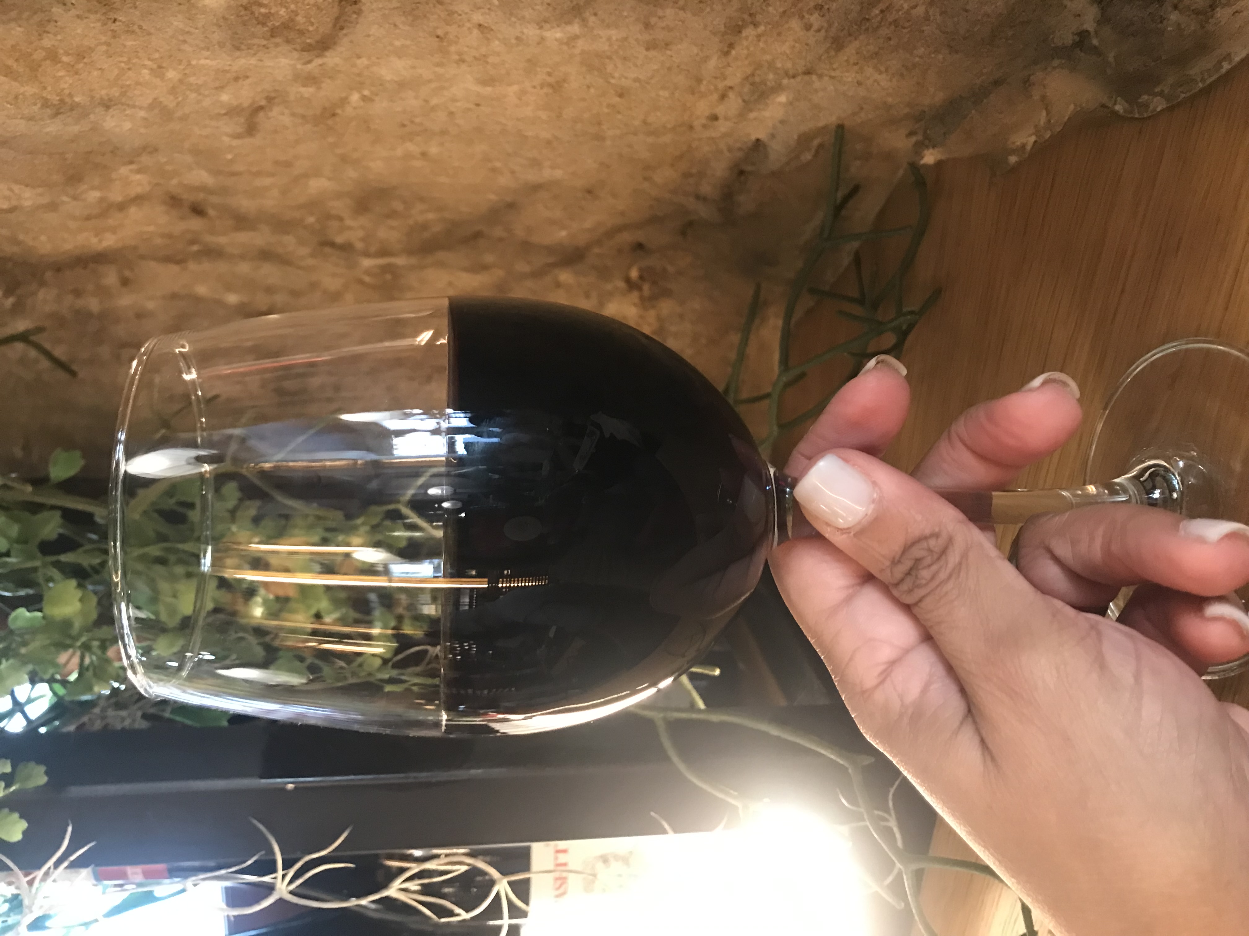 Copa de vino tinto sostenida frente a una pared de piedra en un lugar íntimo