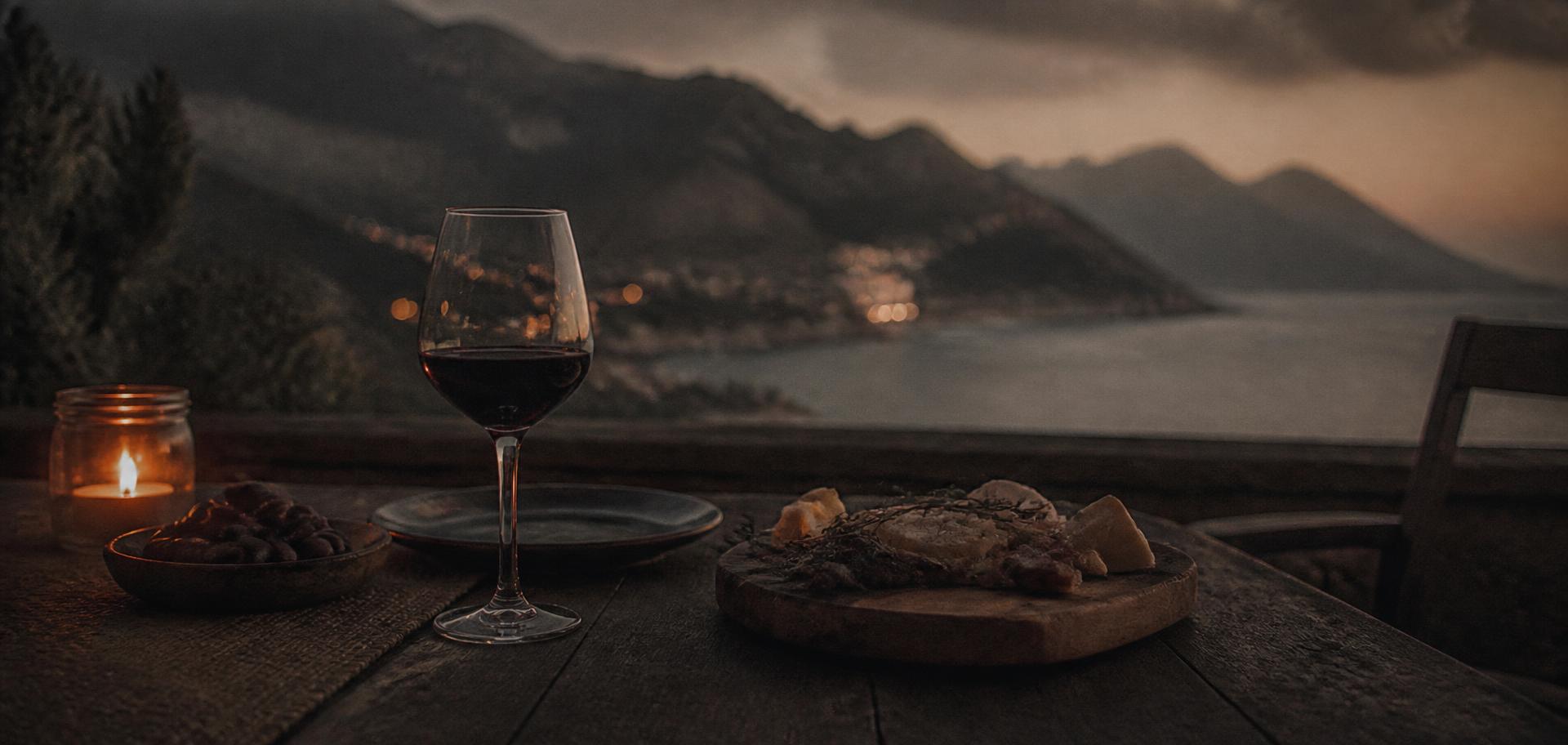Mesa con una copa de vino y una vela frente a un paisaje mediterráneo al anochecer
