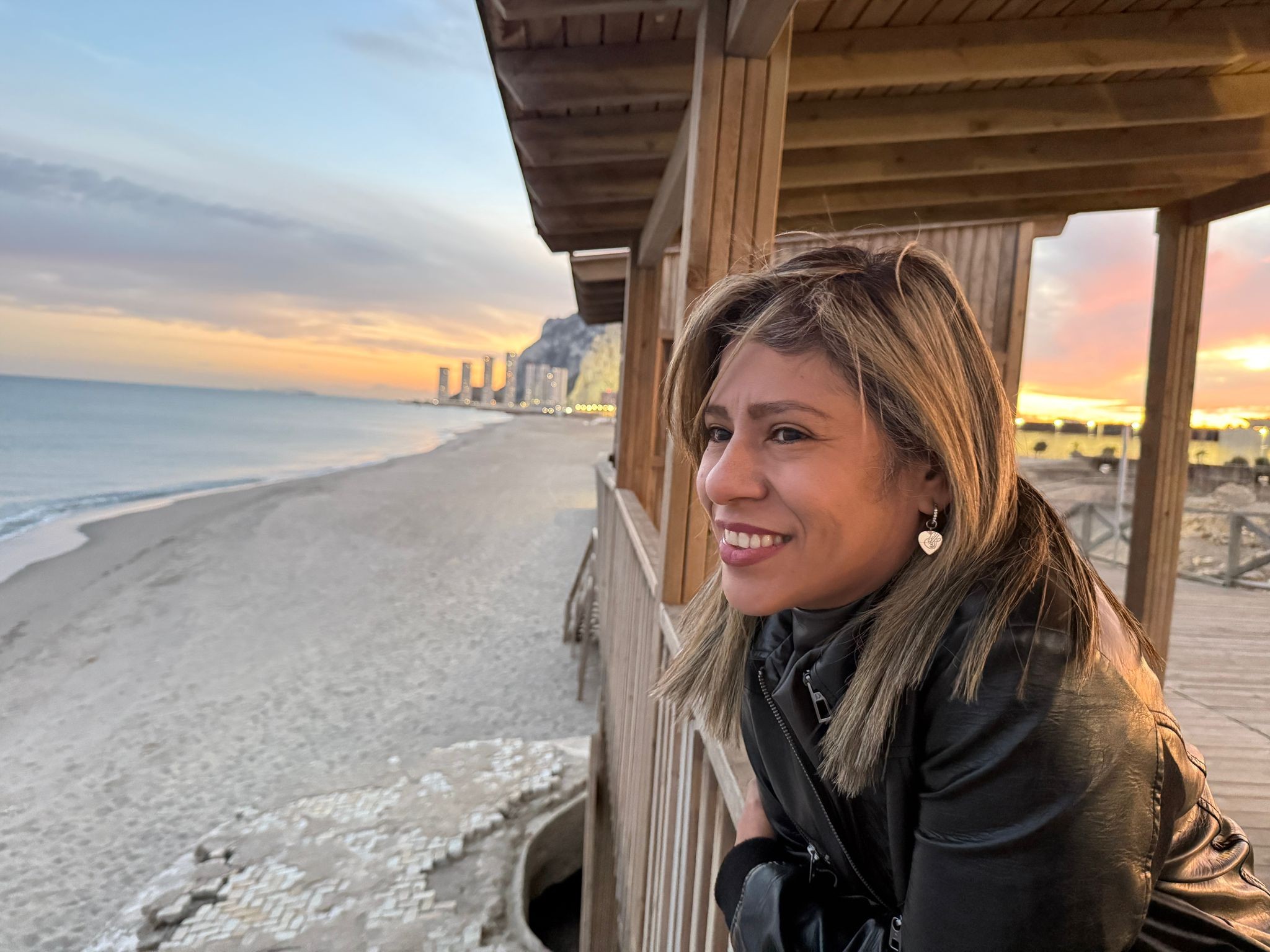 Yfigenia Moreno mirando el mar al atardecer desde una caseta de madera en la playa
